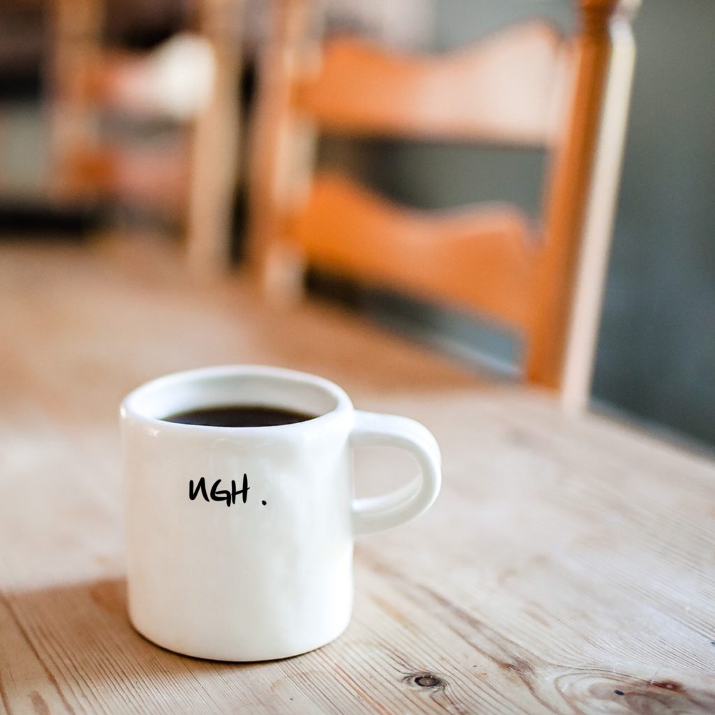 Cup of coffee on table that says UGH. 